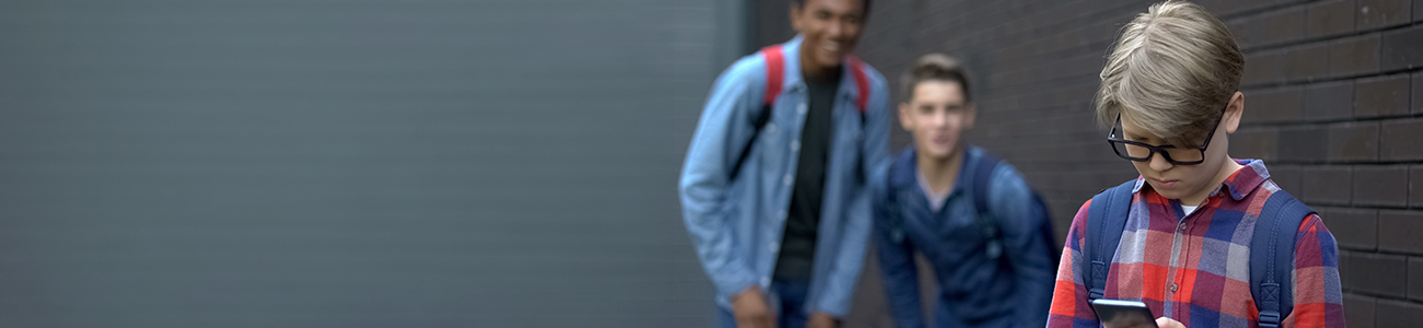 Middle school kid reviewing phone while schoolmates mockingly smile in background