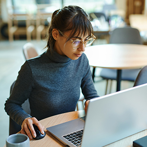 Staff member concentrating on screen and typing on laptop while sitting at desk at workplace