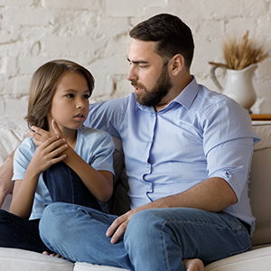 Serious father listen to his pre-teen little son talking seated on sofa at home