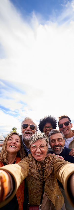 Cheerful vertical selfie of a group of mature people looking at camera happily, taking photos during their family trip together.