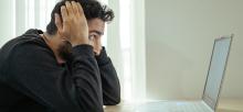 A man sits staring at his laptop with hands beside his head in regret as his online account has been compromised